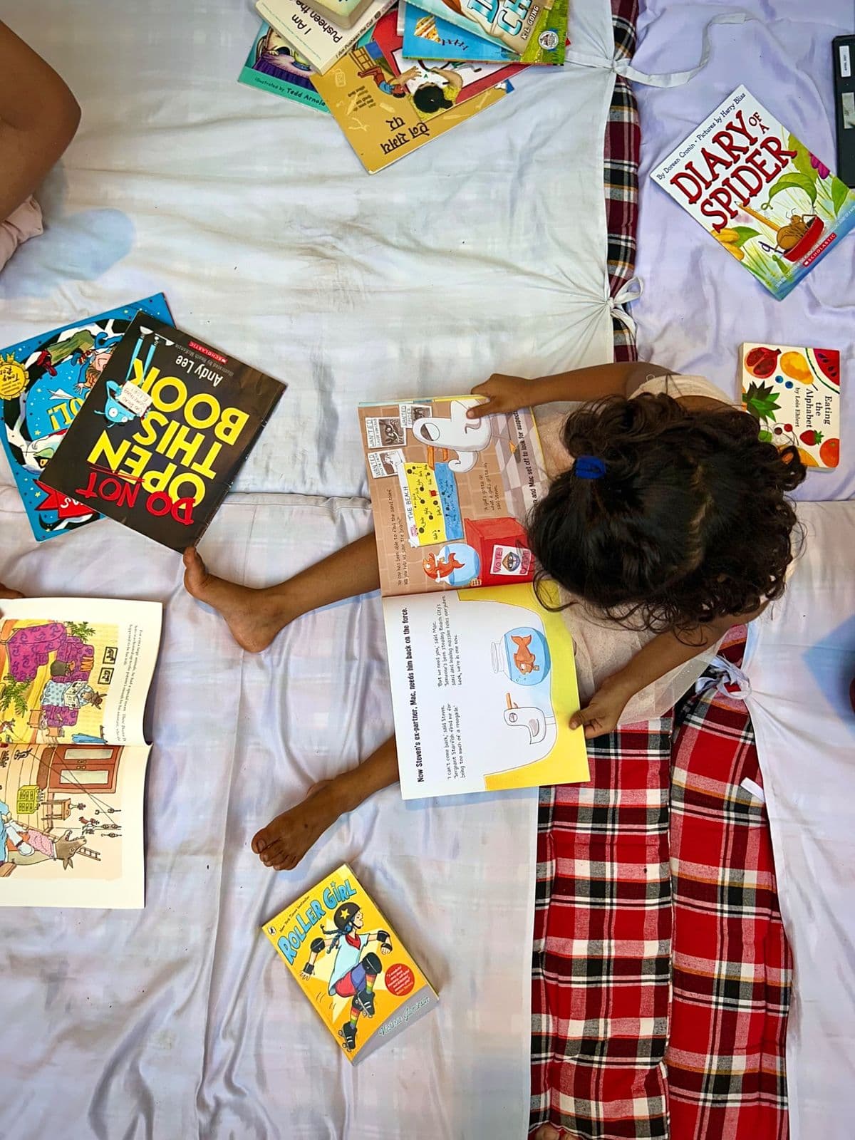 A girl lying on a quilt surrounded by picture books, reading