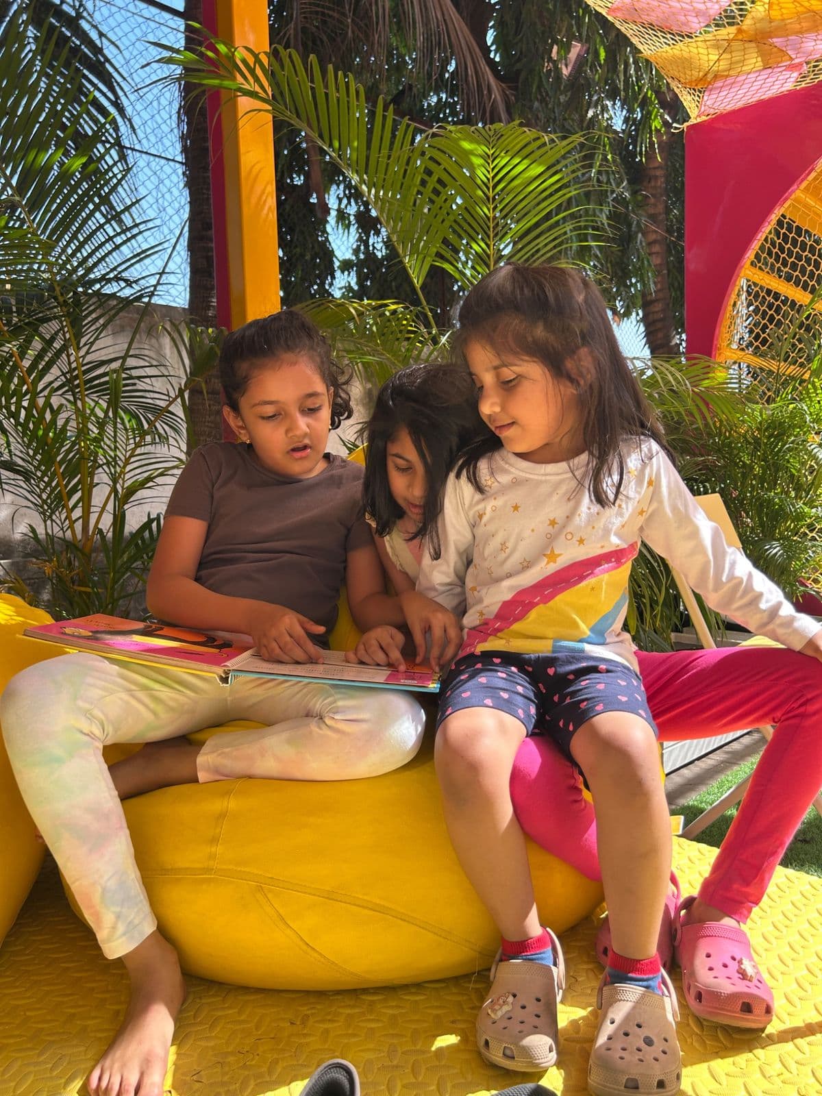 Three girls sharing a picture book on a yellow beanbag