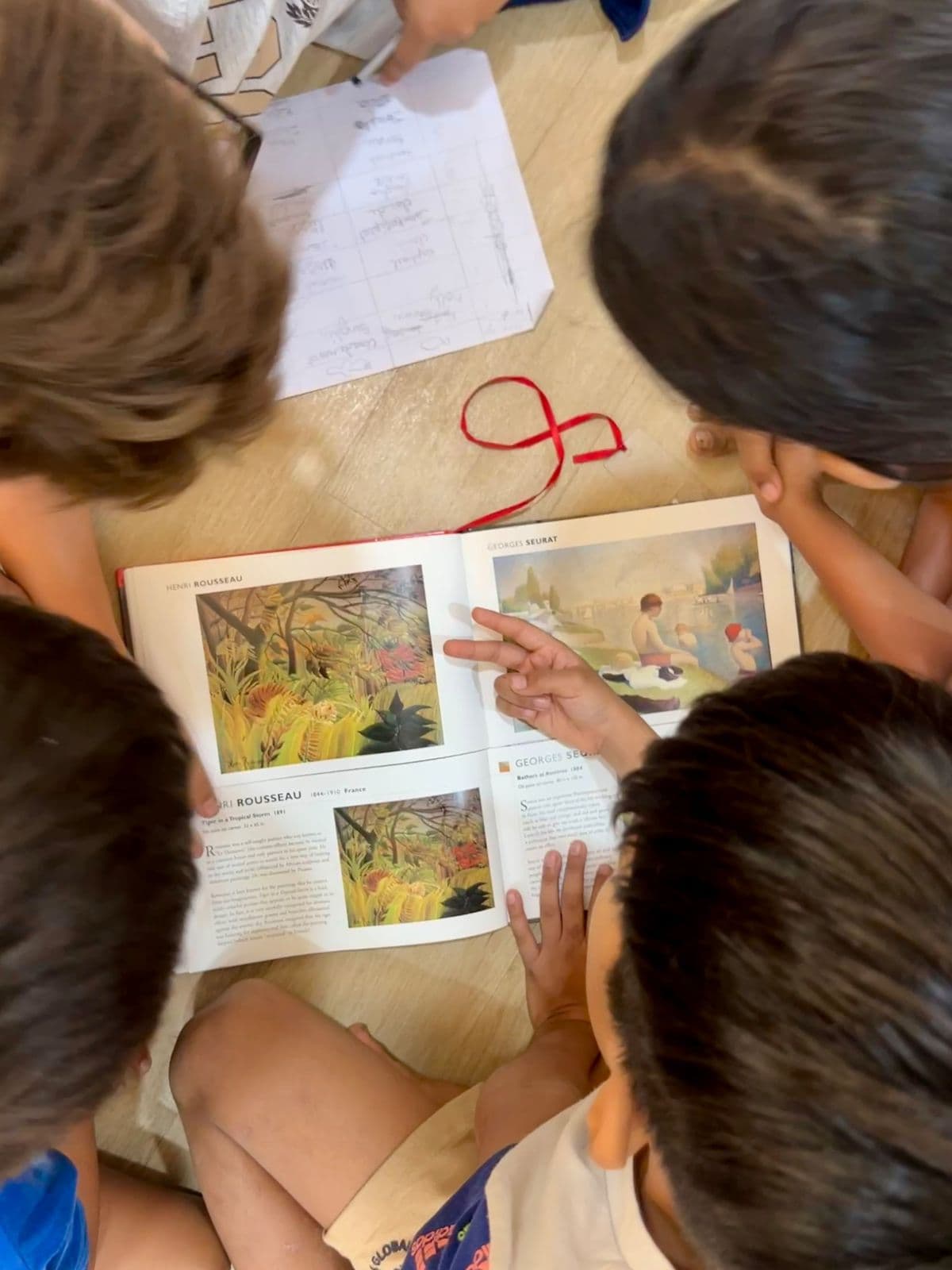 Children leaning over an open art book, pointing at a painting