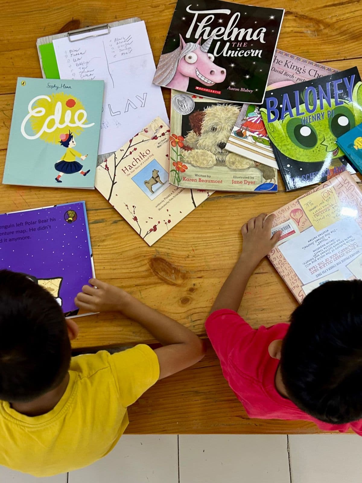 Two children at a wooden table spread with picture books
